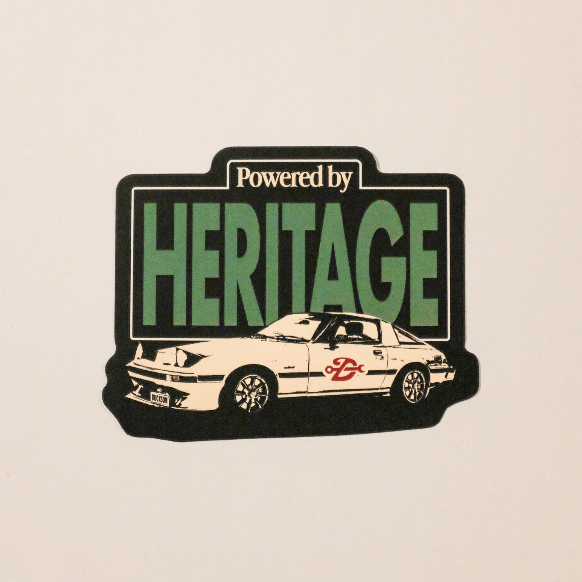 Sticker with 'Powered by Heritage' text and a car illustration on a beige background